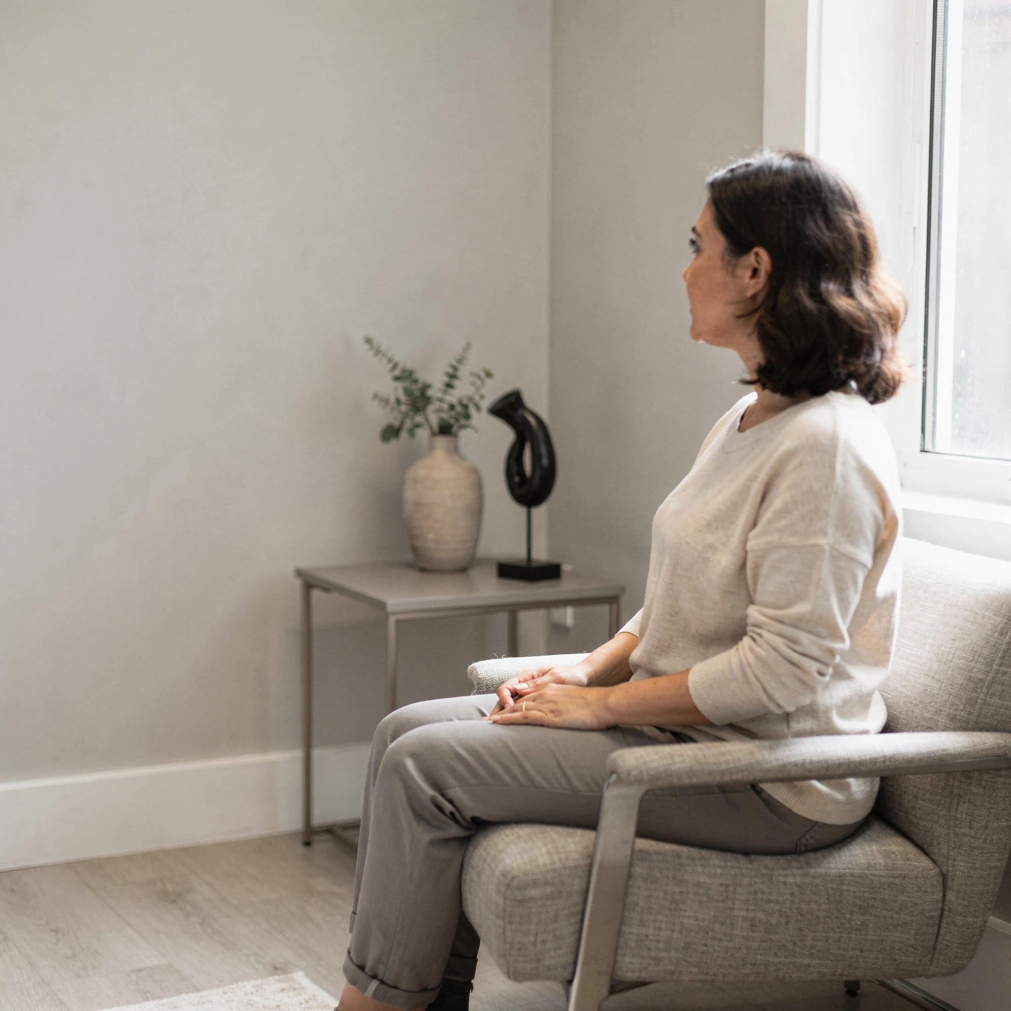 Woman sitting on a couch in a calm, minimalist office with a window and decorative side table